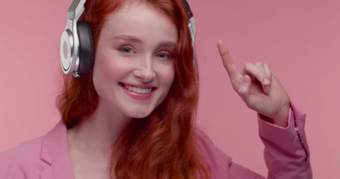Attractive red Haired woman putting on her Big Headphones, enjoying popular Songs. Listening to Favorite music and looking satisfied. Happy woman with good Mood. Having fun at Studio.