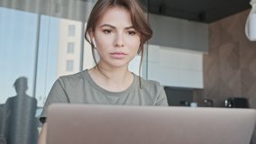 A good-looking young woman with earbuds is working while using her laptop computer sitting at home