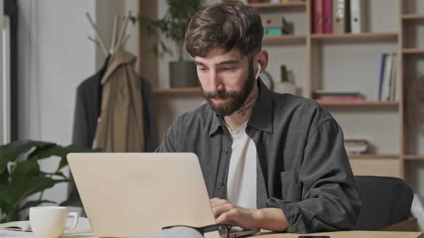 A focused young digital artist in casual clothes is working with his laptop computer sitting in the office | Shutterstock HD Video #1055568038