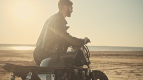 A brutal happy young man rolls a motorcycle while walking on the beach