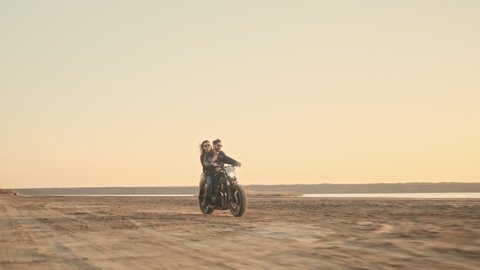 An attractive young couple man and woman are riding on a motorbike together on the beach