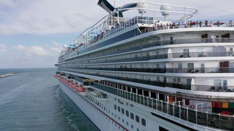 Miami, May 2019. Carnival Cruise liner sailing to Atlantic ocean. People on upper deck celebrates vacation. Water transportation. 4K aerial view of stern of the cruise ship leaving cruise terminal