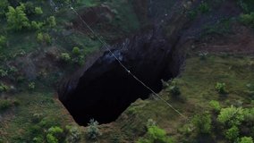 Aerial footage of a massive natural pit with a rope stretched over it, slackline