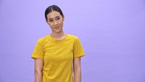 Smiling pretty sportswoman in yellow t-shirt showing ok sign while standing with fitness mat over violet background