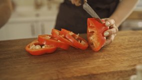 A close-up view of a happy woman in apron is cutting red pepper with her boyfriend at a cozy kitchen