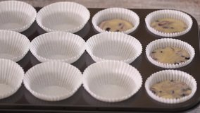 Pouring blueberry batter into muffin cups. Woman baking blueberry muffins.