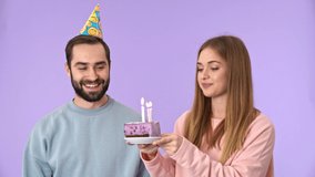 Joyful young lovely couple having fun on birthday party over purple background