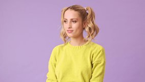 The beautiful blonde in a yellow sweater remembered that she had forgotten to do something important, and realized that she could not do anything about it in an isolated studio on a purple background.