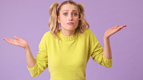 A pretty forgetful blonde in a yellow sweater is trying to find something in her pockets, but can not do it in an isolated studio on a purple background