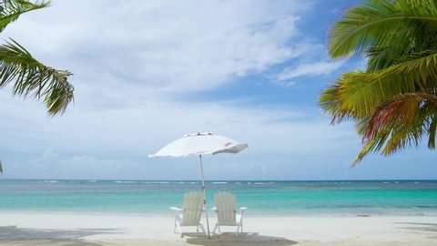 Beach holidays on vacation in the Dominican Republic. Beach loungers and a parasol on a beautiful white beach of the Caribbean. Tropical palm trees frame the video. Without people copy space.