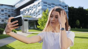 Beautiful girl talking on video call with a friend on the background of a modern building. Sunny day summer