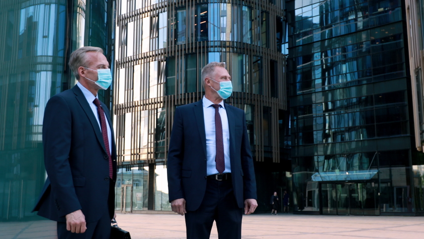 Two businessmen in medical mask meet a businesswoman also wearing a mask and use elbow bumps instead of handshake. Modern office building on the background Royalty-Free Stock Footage #1055581442