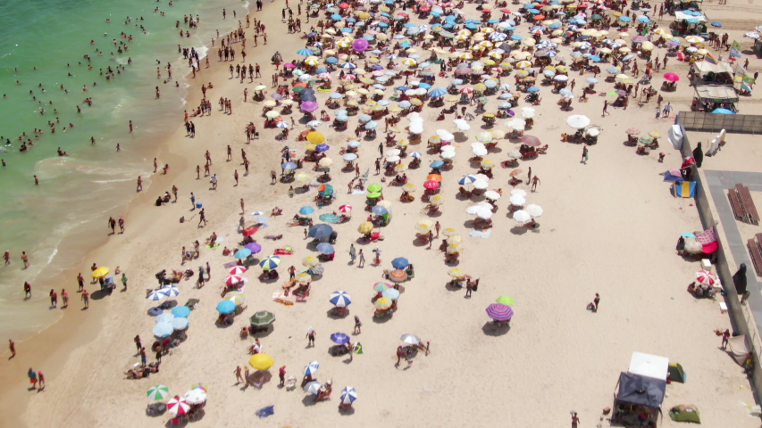 Rio de Janeiro, Brazil, flyover shot of Copacabana Beach showing colourful sun umbrellas and people bathing in the ocean during summer. Royalty-Free Stock Footage #1055581706