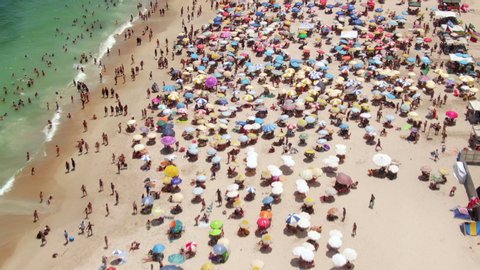 Rio de Janeiro, Brazil, flyover shot of Copacabana Beach showing colourful sun umbrellas and people bathing in the ocean during summer.