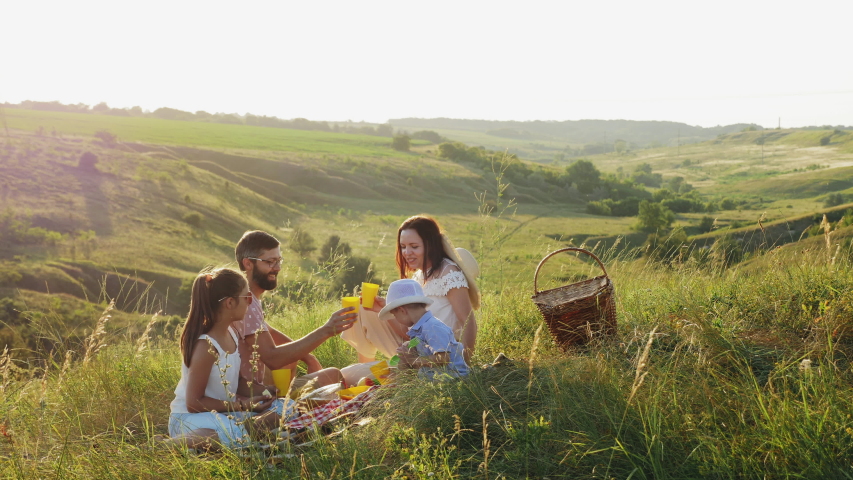 A family of four have fun together on a picnic in nature, children and parents smile, eat and drink Royalty-Free Stock Footage #1055584439