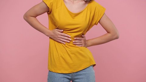 Close up cropped young illness woman girl body in yellow t-shirt put hand on abdomen period pain isolated on pastel pink background studio. People lifestyle medical healthcare gynecological concept