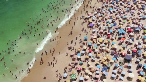 Rio de Janeiro, Brazil, aerial view of busy Copacabana Beach showing colourful sun umbrellas and people bathing in the ocean during summer.