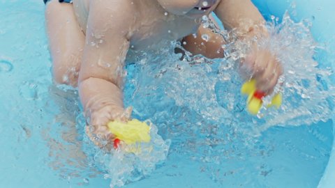 Childs hands with yellow rubber ducks splashes water during swimming in pool outdoors at summer. Little baby boy having fun. Concept of healthy lifestyle, family, leisure in summer. Slow motion.