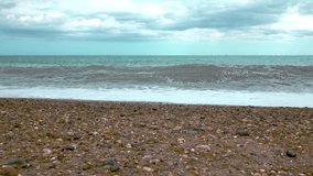 Approaching from the ground to the waves of the ocean. Beach waves in slow motion in Brighton, England. Sea waves in a cloudy and windy day in 4K.