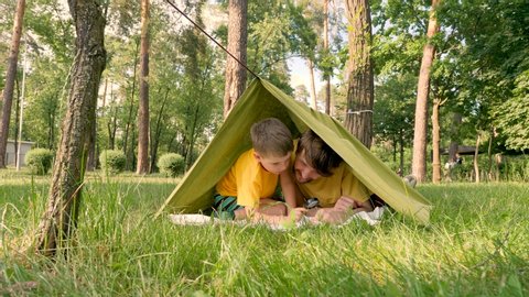 Father with son in tent on green grass discovering flora and fauna. Father with son lying in camp tent. Two travelers having fun in tent. Traveling close to home. One parent family