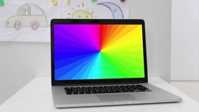 a panning video of a laptop with a hypnotic rainbow pattern in kid's room. 