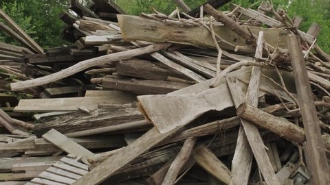 Pan right view of leftover planks and tree branches stacked in pile in yard (slow motion)