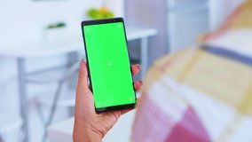 Woman watching video content on phone with green screen in kitchen. Green screen chroma mock up isolated mockup background ready to be replaced with your text, logo or advertisement. Using internet