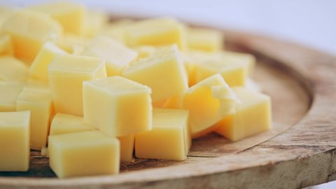 Yellow diced cheese is rotating on a wooden plate. Cubes of cheese