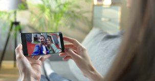 Girl talking on video conference on smartphone in living room. Woman having video conversation with joyful Caucasian male and female friends who are walking outdoor on cellphone. Online chat concept