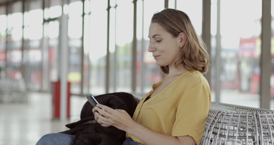 Pretty female sitting in airport terminal using smart phone and waiting for flight