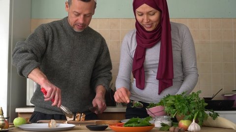 Middle-aged happy arabic couple together preparing food in a kitchen. Authentic muslim husband and wife cooking together at home