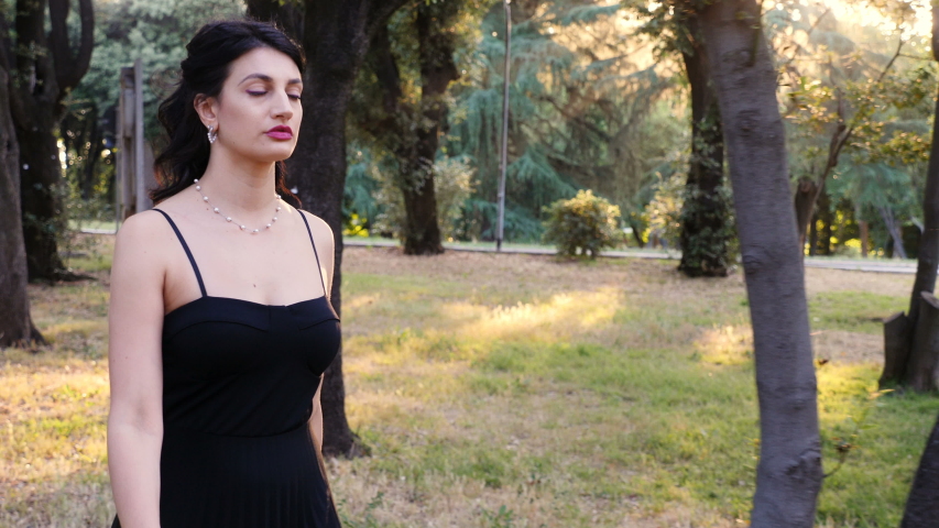 Confident attractive woman wearing sexy black dress walking at park