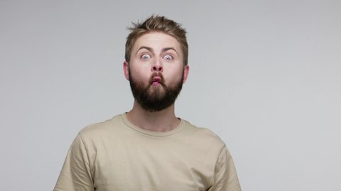 Surprised funny bearded guy looking at camera with surprised big eyes, making fish face grimace pout lips, smooching choking with idiotic duck expression. studio shot isolated on gray background