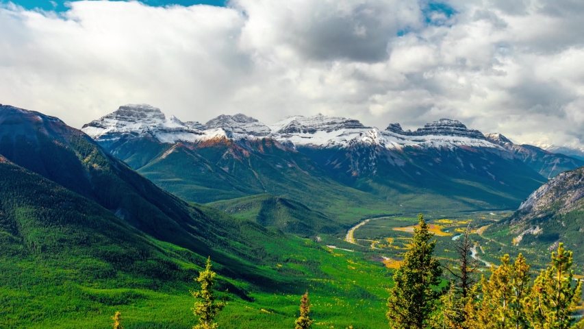PAN IN Perfect Picturesque Snow Covered Mountain range with a large valley in the Colorado Rocky Mountains with snow clouds, PAN IN Gateway to Paradise Banff National Park Mount Bourgeau time Lapse 4K Royalty-Free Stock Footage #1055633927