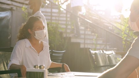 Waitress with protective medical mask and gloves serving guest with cocktails in outdoor restaurant. Opens new concept after quarantine, 4K