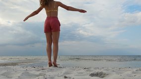 4K video of young fitness woman doing jumping jacks and  active exercises outdoors at coast of Baltic sea in Germany