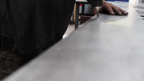 Close-up Shot Of A Worker Drilling A Hole On A Metal Sheet. Close up hand held video as man’s hands are drilling holes on a steel sheet.