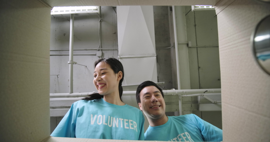 Young asian male and female volunteer putting food in a donation box together as charity workers and members of the community work to the poor during the Coronavirus pandemic. social distance concept. Royalty-Free Stock Footage #1055640857