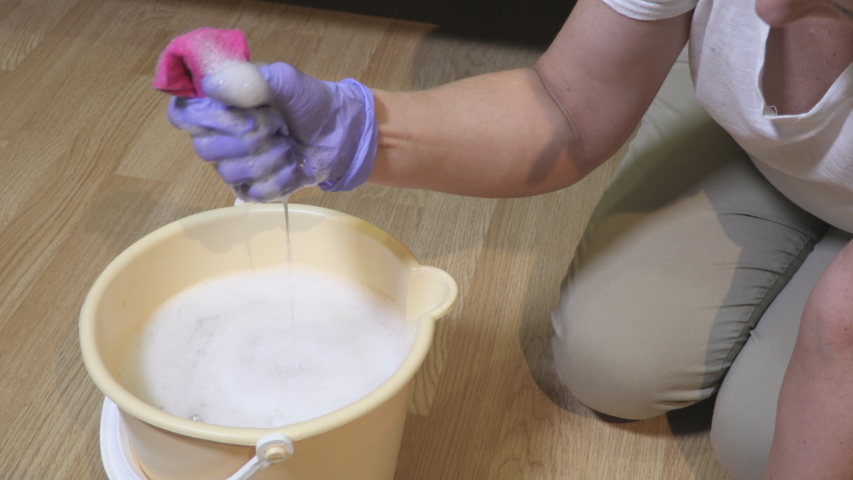 Woman washing and squeezing rag in bucket at home