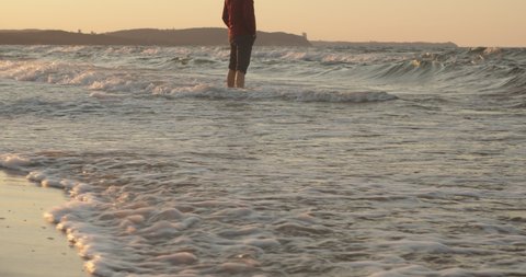 Man Stands in Sea Water on a Sandy Beach, Sea Waves Wash the Legs of a Man. Slow Motion