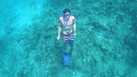 SLOW MOTION, UNDERWATER, CLOSE UP: Male snorkeler ascends from the depths and to the surface of the deep blue sea. Active man on summer vacation in Maldives snorkels around the scenic turquoise ocean.