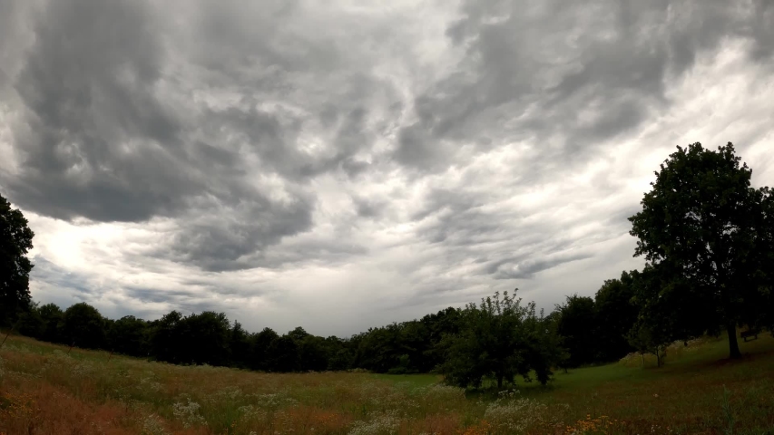 Wide angle time lapse of turbulent rain clouds approaching over a rural meadow