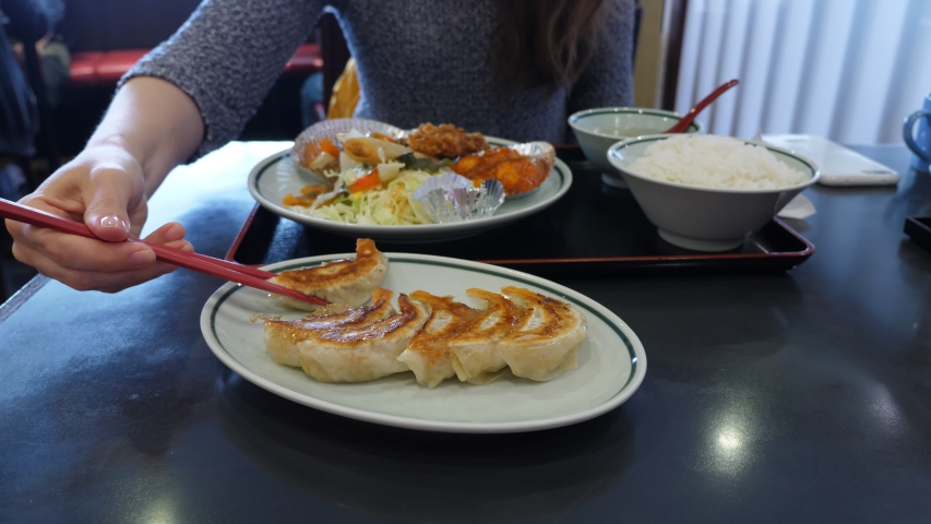 Tourist woman hold one fried Gyoza by chopsticks against platter, then eat it. Traditional dumplings served at Japanese restaurant as side dish with lunch set