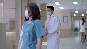 In Hospital, Busy Doctors with face mask talking While walking in corridor. In Background Patient and staff walking in ward area. concept medical people life in Modern clean Medical Facility.
