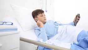 child in hospital with the mobile phone and earphones lying alone in bed