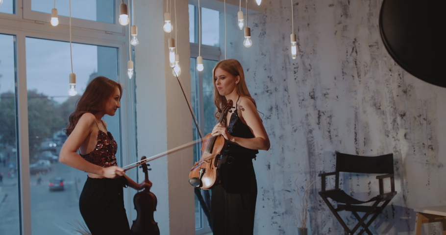 Beautiful female musicians having fun and dancing with violins at window in studio. Slowly in 4K