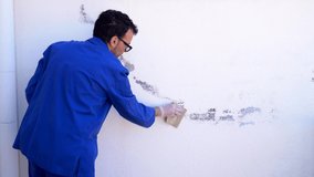 Painter scrubbing the white wall of the house with sandpaper. Stock video of mature man reforming the terrace of the house.