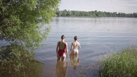 Two female friends swimming in river during sunny day