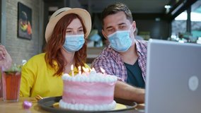 social distance, joyful man and woman in medical masks to protect themselves from virus and infection during pandemic have fun chatting with friends via video chat on laptop celebrate birthday