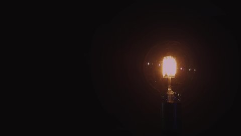 Incandescent light bulb isolated on black background. Glass and metal base. Lights up brightly with blinking and fades out. Edison lamp. 4K resolution